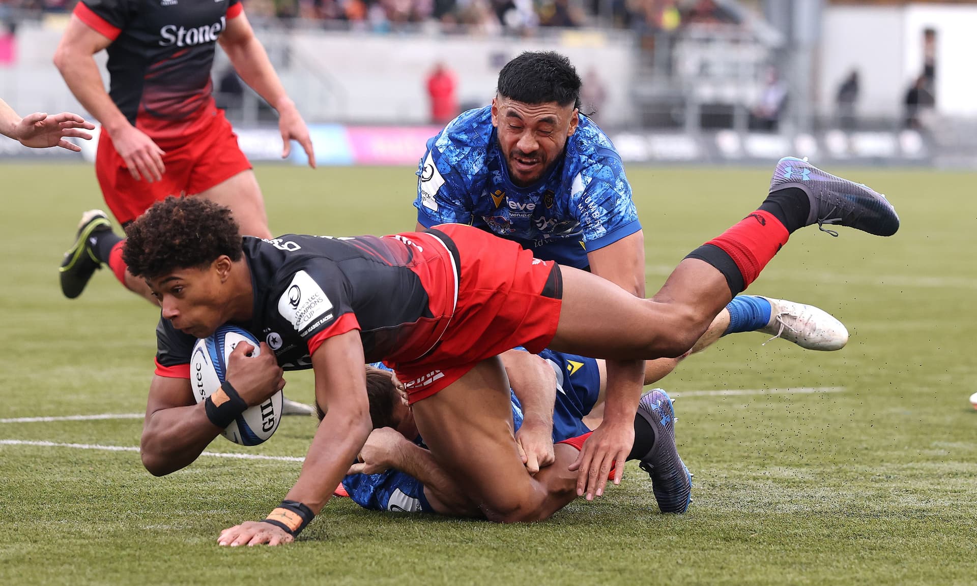 Noah Caluori of Saracens is held by Alex Newsome and Irae Simone