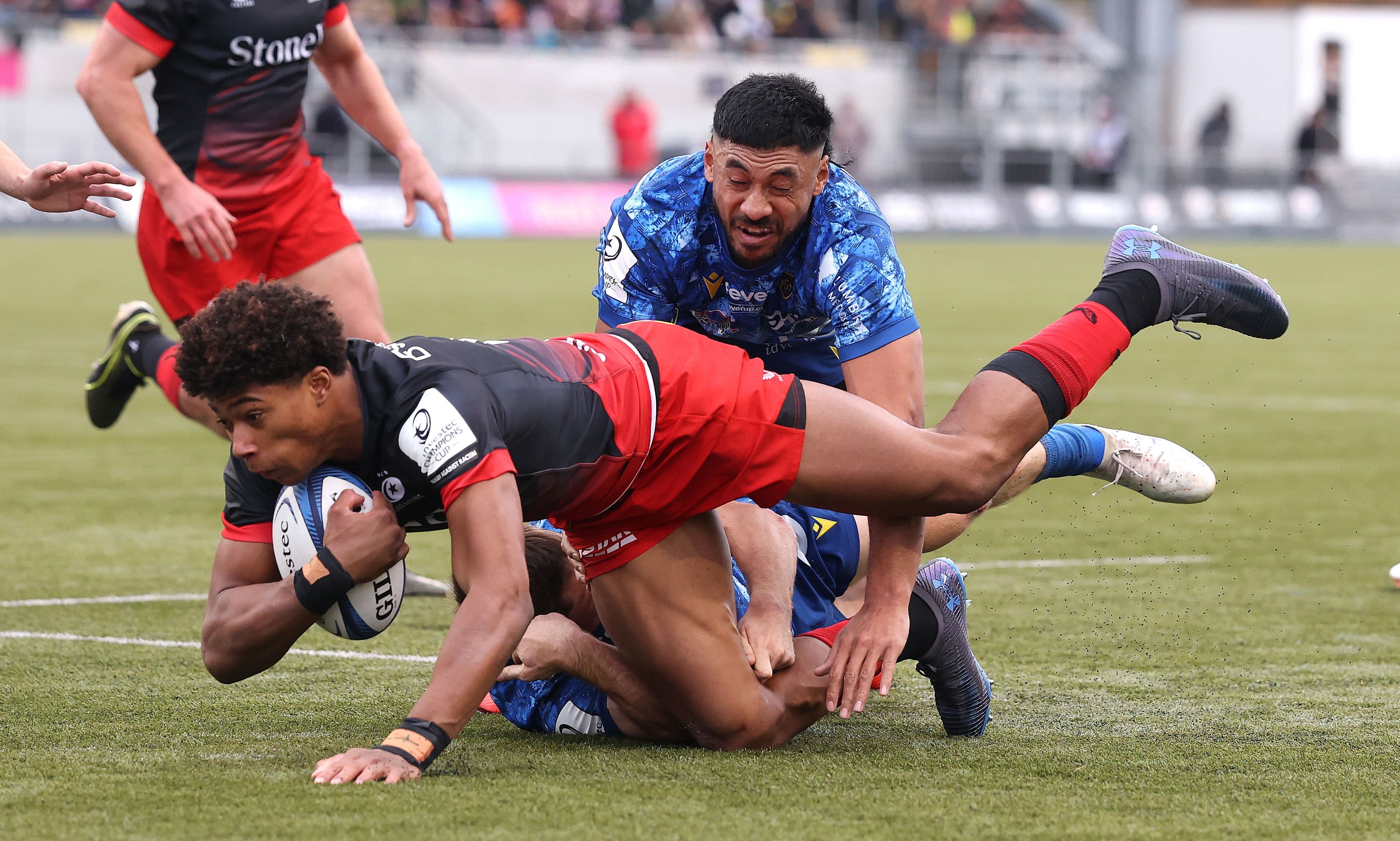 Noah Caluori of Saracens is held by Alex Newsome and Irae Simone