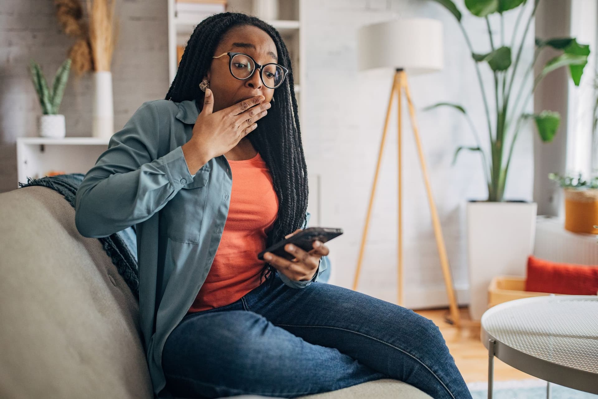 Woman holding smartphone playing mobile game celebration success at home.
